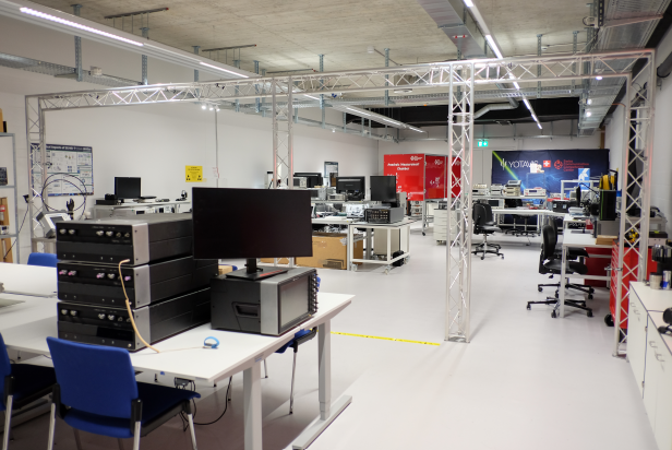 SwissCCC open lab with multiple workstations, RF and EMC test equipment, and Yotavis branding